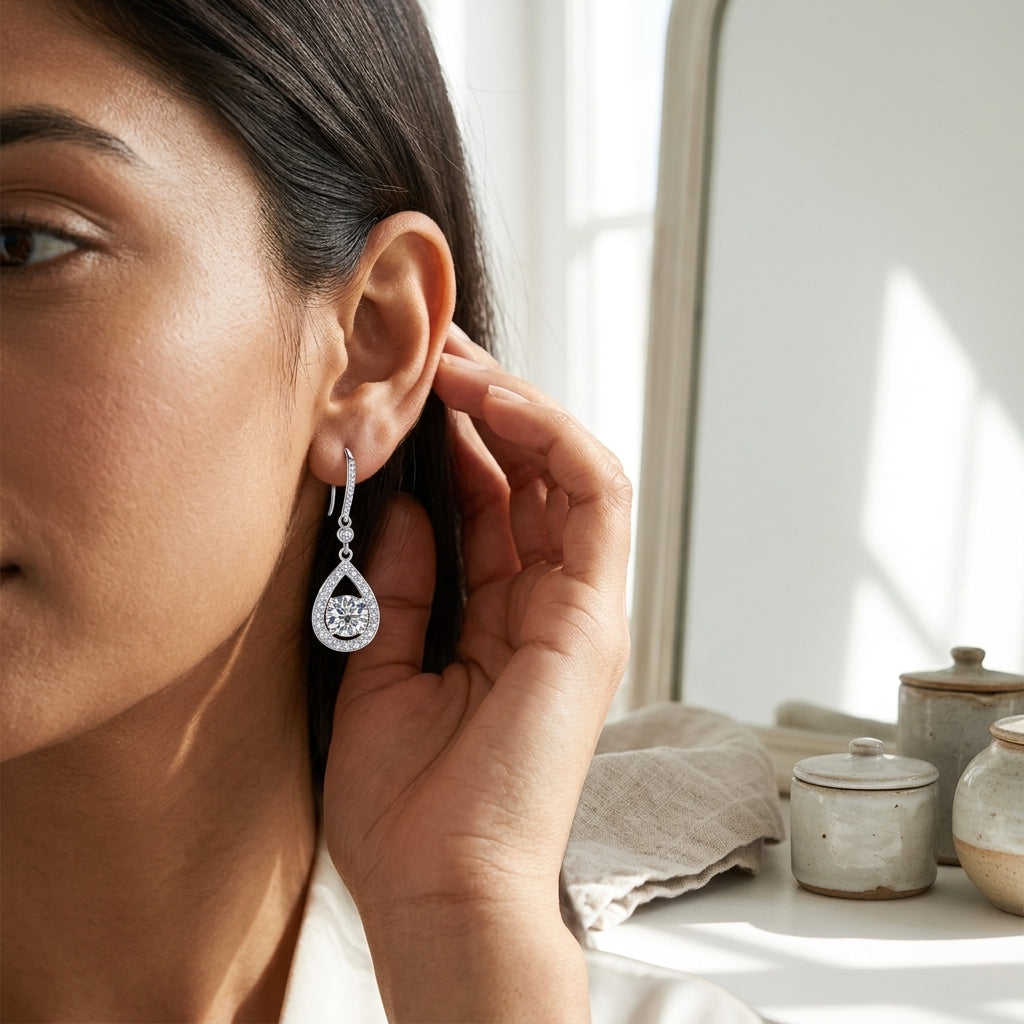 Woman touching a 1 carat teardrop moissanite dangle earring near a sunlit window