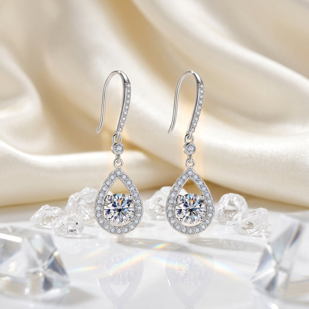Pair of teardrop moissanite dangle earrings displayed on cream satin with crystal accents