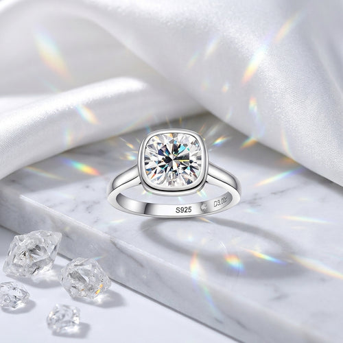 Cushion-cut moissanite bezel engagement ring displayed on white satin and marble