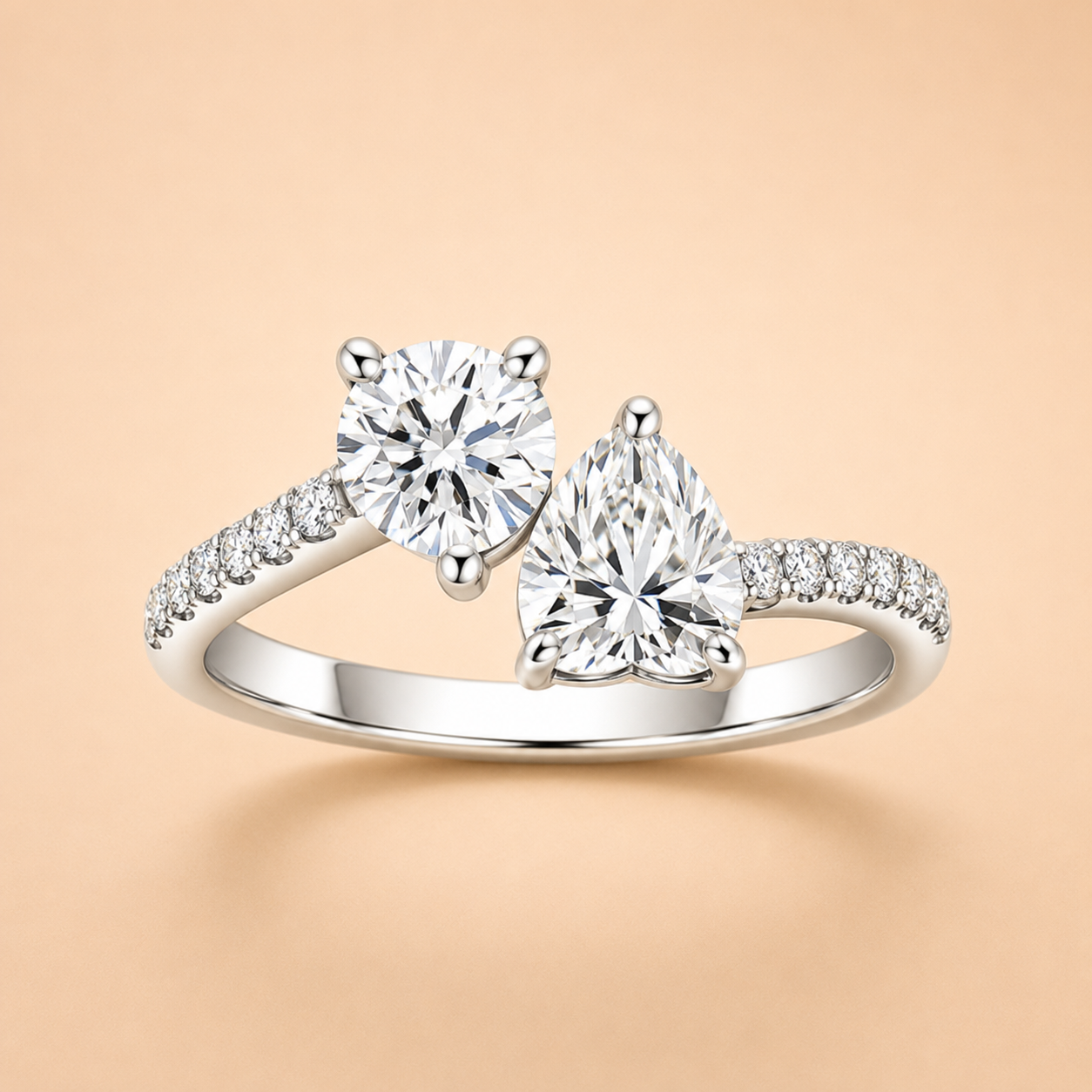 Two-stone moissanite engagement ring with round and pear-cut stones and pavé shoulders