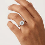 Close-up of a cushion-cut moissanite engagement ring worn on the hand.