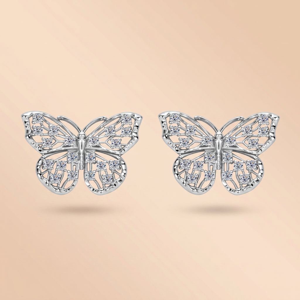 Pair of 1.6 MM butterfly moissanite stud earrings in silver on a cream background