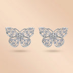 Pair of 1.6 MM butterfly moissanite stud earrings in silver on a cream background