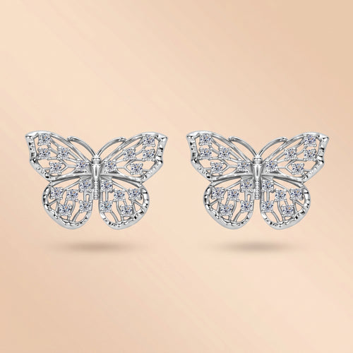Pair of 1.6 MM butterfly moissanite stud earrings in silver on a cream background