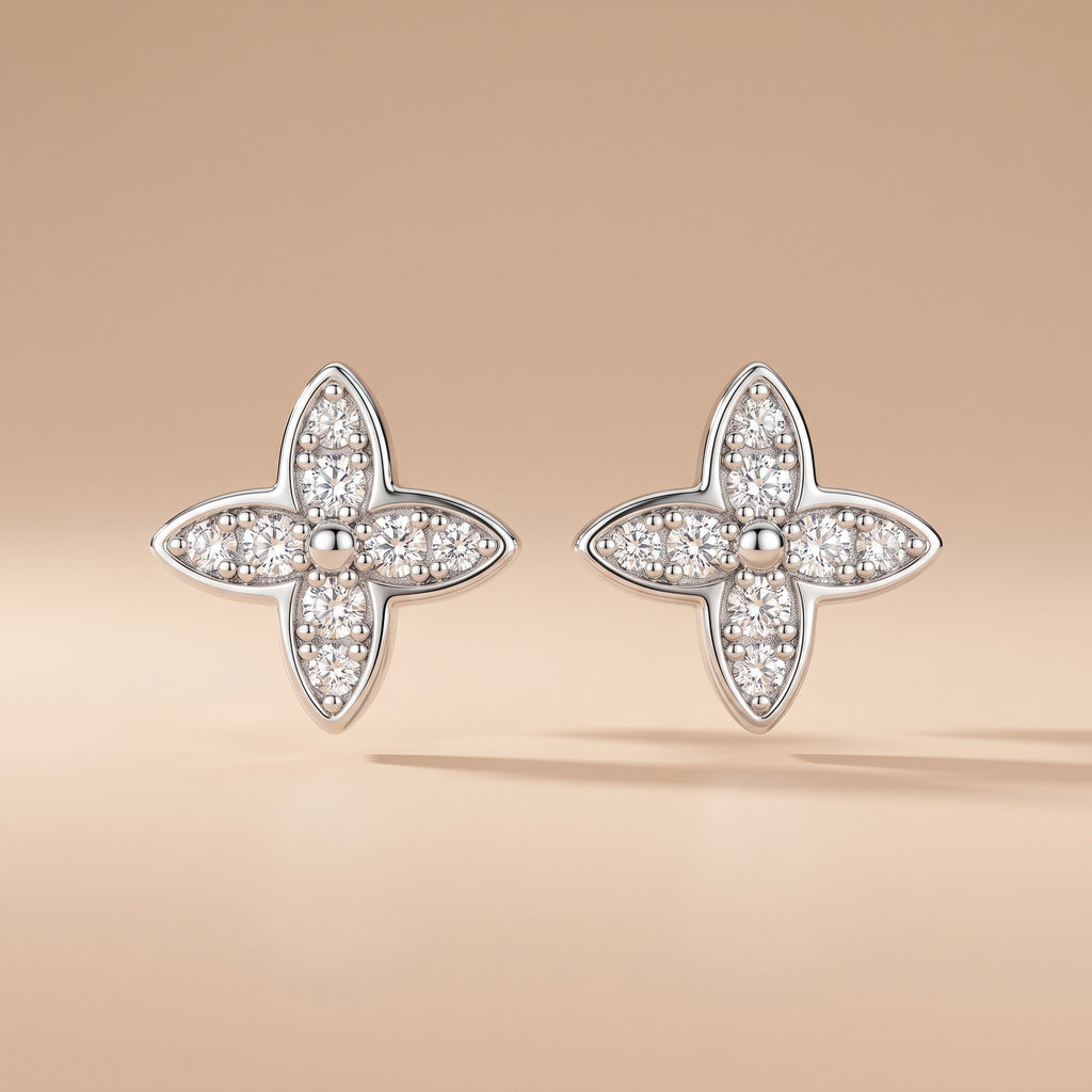Pair of four-leaf moissanite stud earrings in sterling silver on a beige background
