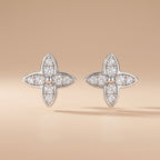 Pair of four-leaf moissanite stud earrings in sterling silver on a beige background