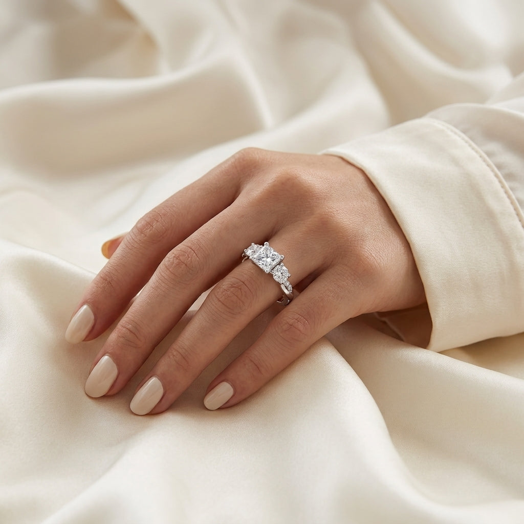 Woman wearing a princess-cut moissanite engagement ring on cream satin