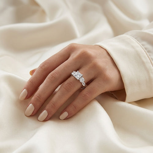 Woman wearing a princess-cut moissanite engagement ring on cream satin