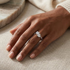 Woman wearing a twin-stone moissanite engagement ring on a neutral linen background