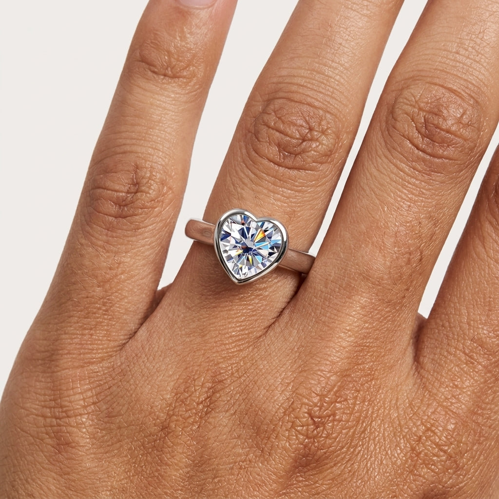 Close-up of a heart-cut moissanite bezel engagement ring worn on the hand