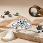 Heart-cut moissanite bezel ring displayed on stone with satin ribbon and crystal accents