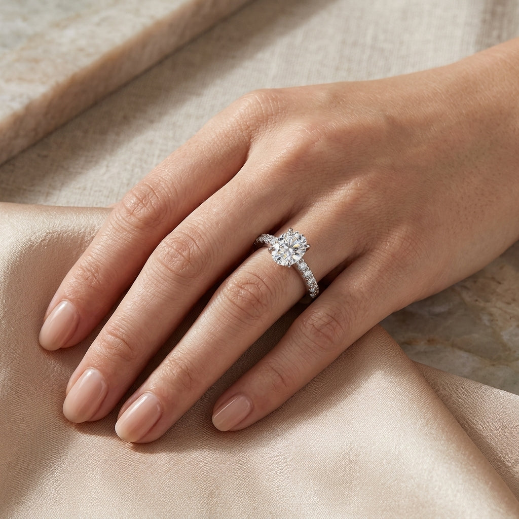 Oval-cut moissanite pavé engagement ring worn on a hand resting on satin