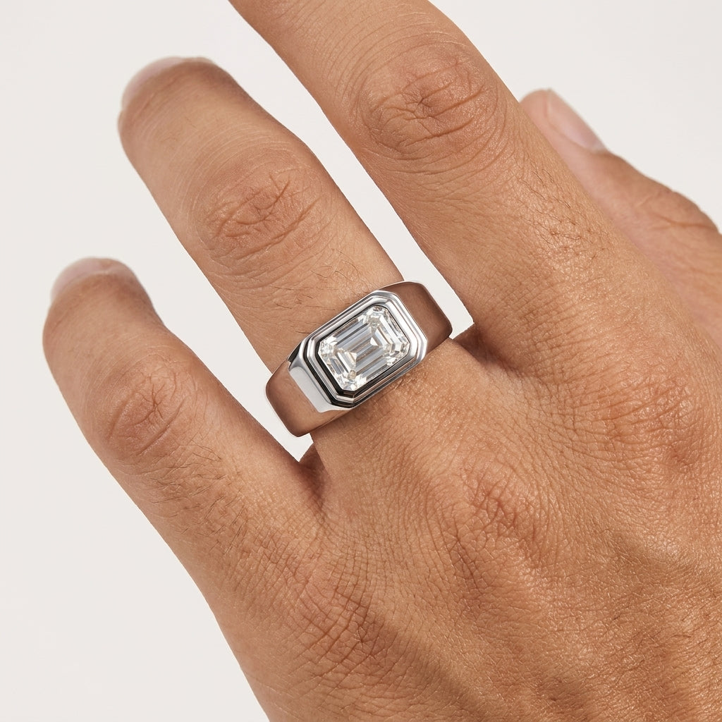 A silver-toned ring with a rectangular emerald-cut clear gemstone, shown worn on a person's finger against a light neutral background.