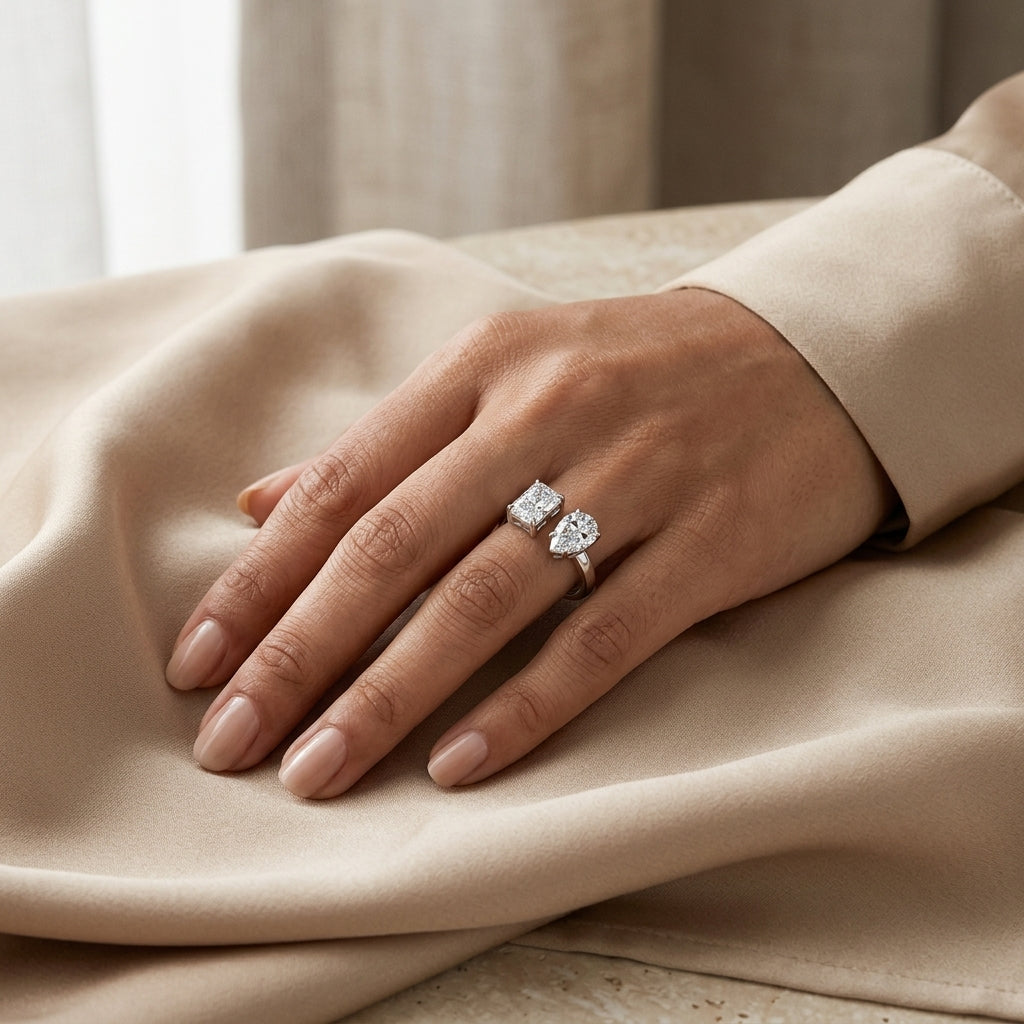 Radiant and pear-cut twin moissanite ring worn on a hand resting on cream satin