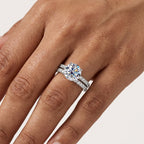 Close-up of a round-cut moissanite engagement ring set worn on the hand.