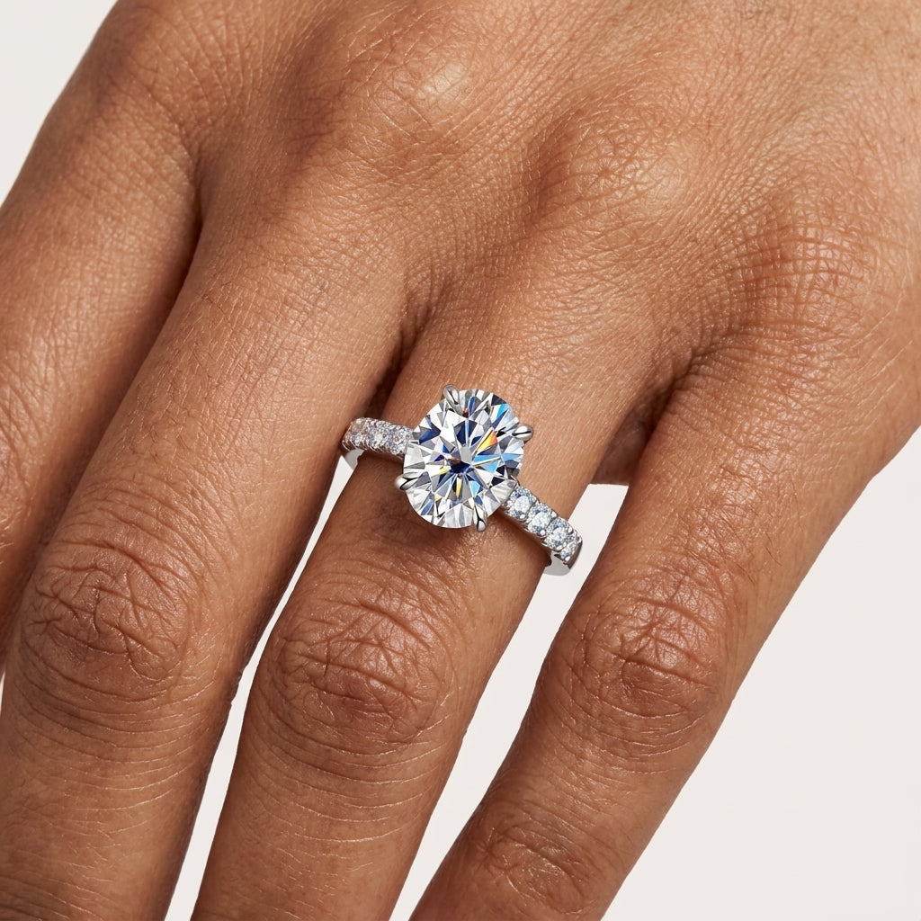 Close-up of a 3 CT oval-cut moissanite ring with a pavé band worn on the hand.